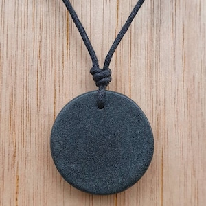 May include: A black round pendant on a black cord necklace. The pendant is made of a smooth, dark material.