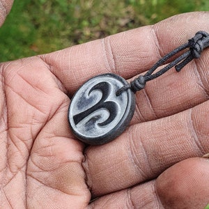 May include: A black cord necklace with a round pendant featuring a carved design of the number three.