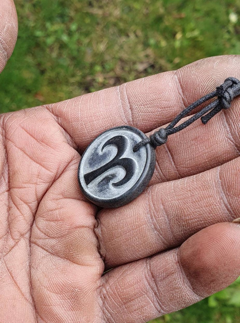 May include: A black cord necklace with a round pendant featuring a carved design of the number three.