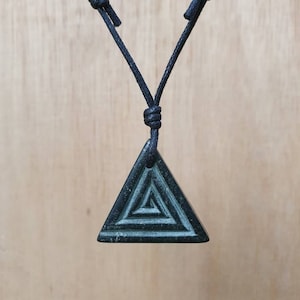 May include: A black cord necklace with a dark green triangle pendant. The pendant has a concentric circle design carved into it.