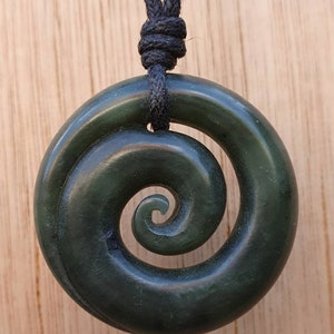 Op de afbeelding: Een donkergroene jade hanger met een spiraalvormig ontwerp, hangend aan een zwart koord.