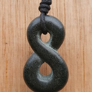Op de afbeelding: Een zwarte stenen hanger in de vorm van een oneindigheidssymbool, hangend aan een zwart koord.