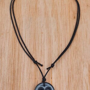 May include: A black cord necklace with a round gray pendant featuring the astrological symbol for Aries.