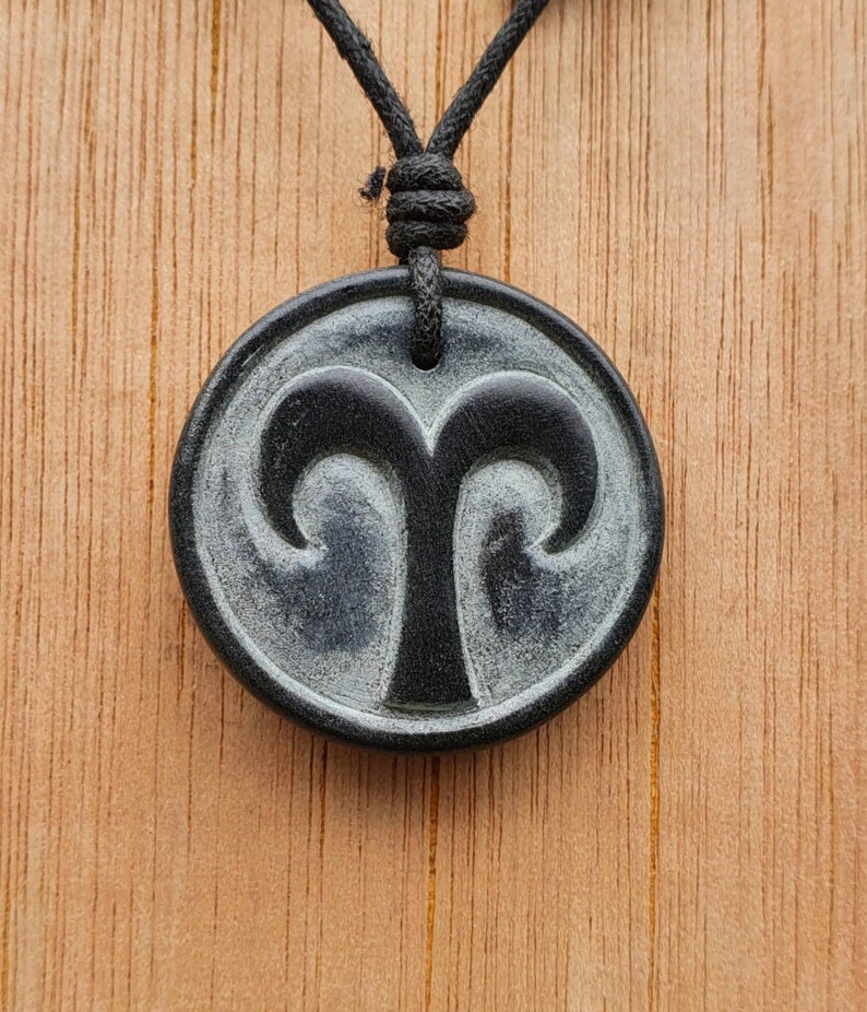 May include: Black and white pendant necklace with a carved ram's head design. The pendant is on a black cord.