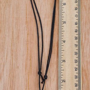 May include: A black cord necklace with a round black pendant featuring a silver Aries zodiac symbol. The pendant is about 1 inch in diameter.