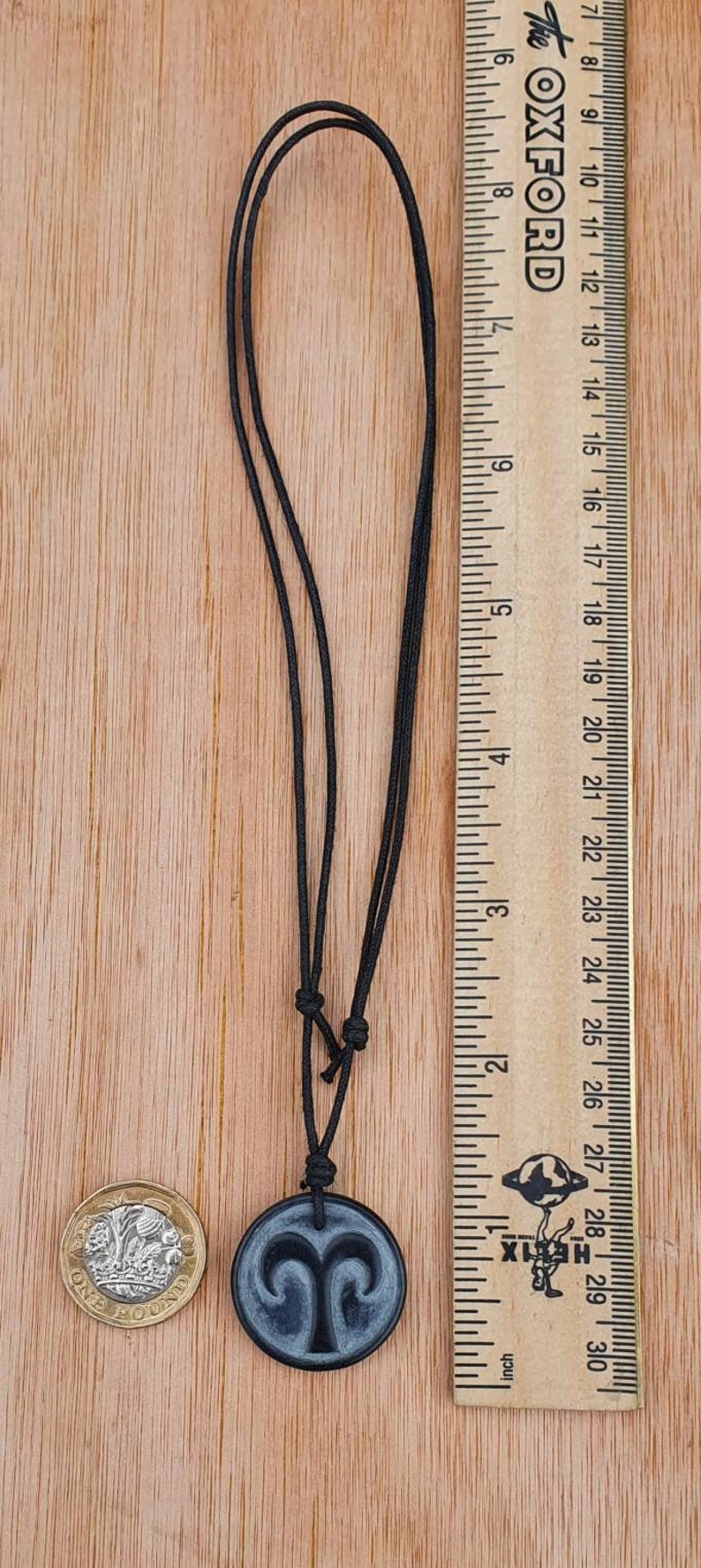 May include: A black cord necklace with a round black pendant featuring a silver Aries zodiac symbol. The pendant is about 1 inch in diameter.