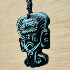 May include: Black pendant necklace featuring a carved image of a deity with a crown and intricate details. The pendant is made from dark stone with a green tint.