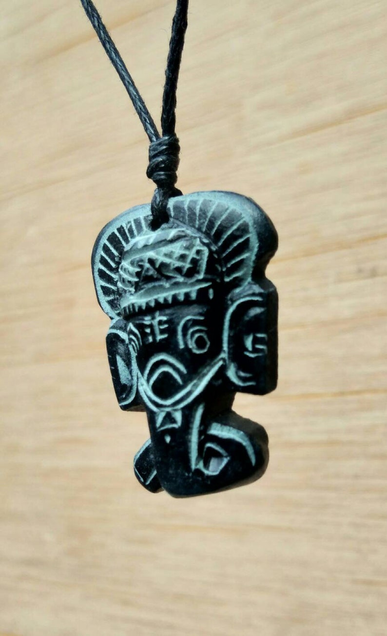 May include: Black pendant necklace featuring a carved image of a deity with a crown and intricate details. The pendant is made from dark stone with a green tint.