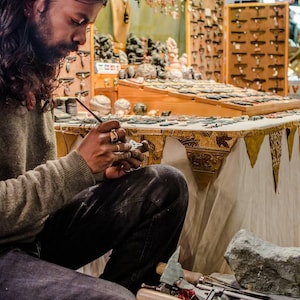 May include: A person working on a stone carving with tools and a piece of stone on a table covered with a white tablecloth. The table is decorated with a patterned fabric.