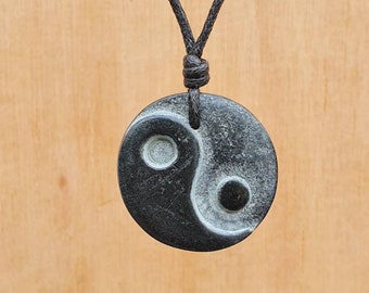 May include: A black and white yin yang symbol pendant on a black cord necklace. The pendant is made of smooth, polished stone.