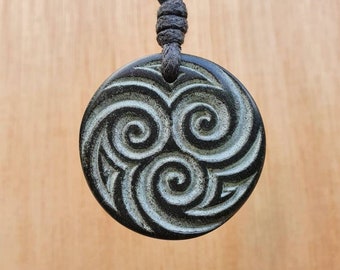 May include: A black pendant necklace with a circular pendant featuring a carved design of three white spirals. The pendant is on a black cord.