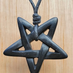 May include: A black wooden pentagram pendant on a black cord necklace. The pendant is intricately carved with a five-pointed star design.