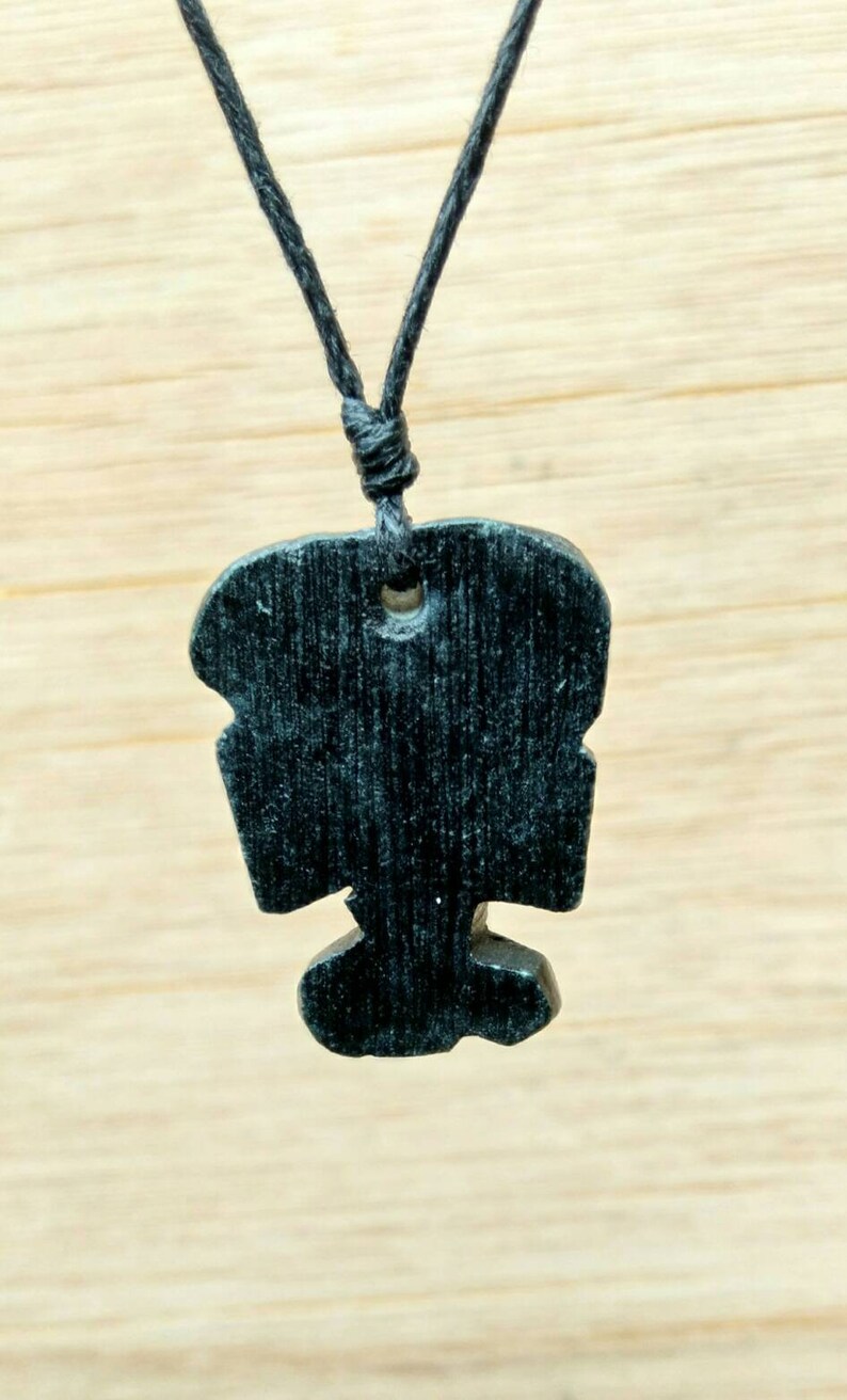 May include: A black wooden pendant with a unique design hangs from a black cord necklace.