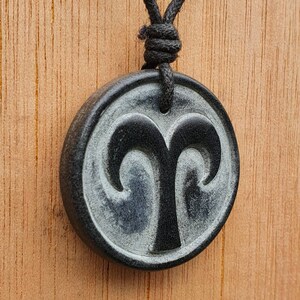 May include: Black and white zodiac pendant necklace with a ram symbol. The pendant is round and has a black cord.