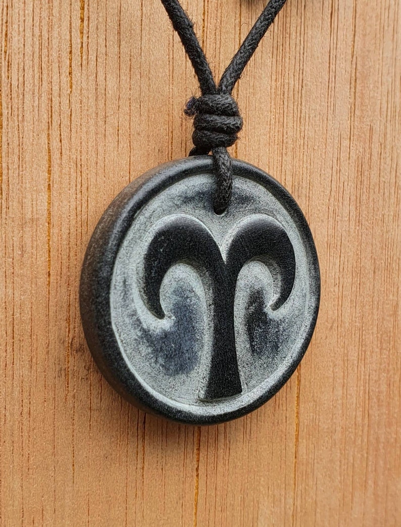 May include: Black and white zodiac pendant necklace with a ram symbol. The pendant is round and has a black cord.