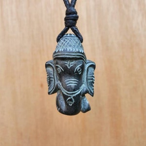 Pode incluir: Um colar com um pingente de pedra preta que representa uma escultura da divindade hindu Ganesha. O colar tem um cord&atilde;o preto.