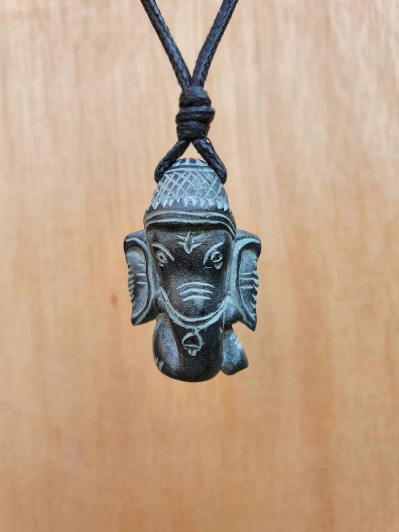 Pode incluir: Um colar com um pingente de pedra preta que representa uma escultura da divindade hindu Ganesha. O colar tem um cord&atilde;o preto.