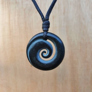 Op de afbeelding: Een zwarte koordketting met een donkergroene jade hanger met een gegraveerd spiraalontwerp.