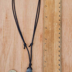 Pode incluir: Um colar de cord&atilde;o preto com um pingente de pedra cinza escuro que apresenta uma imagem esculpida da divindade hindu Ganesha. O pingente tem aproximadamente 5 cm de altura.