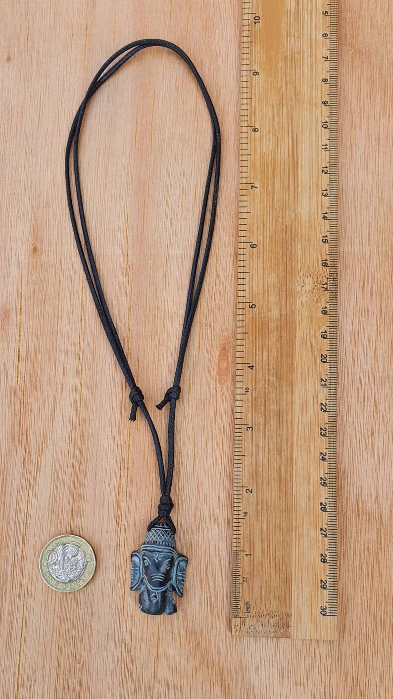 Pode incluir: Um colar de cord&atilde;o preto com um pingente de pedra cinza escuro que apresenta uma imagem esculpida da divindade hindu Ganesha. O pingente tem aproximadamente 5 cm de altura.