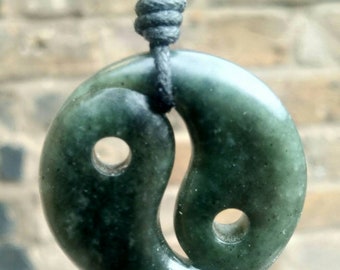 May include: A green jade yin yang pendant on a black cord necklace. The pendant is carved with a yin yang symbol and has a smooth, polished finish.