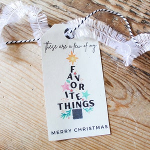 Op de afbeelding: Een wit cadeau-etiket met een zwart-wit koord. Het etiket heeft een kerstboomontwerp met de woorden "Dit zijn een paar van mijn favoriete dingen" en "Prettige Kerst".