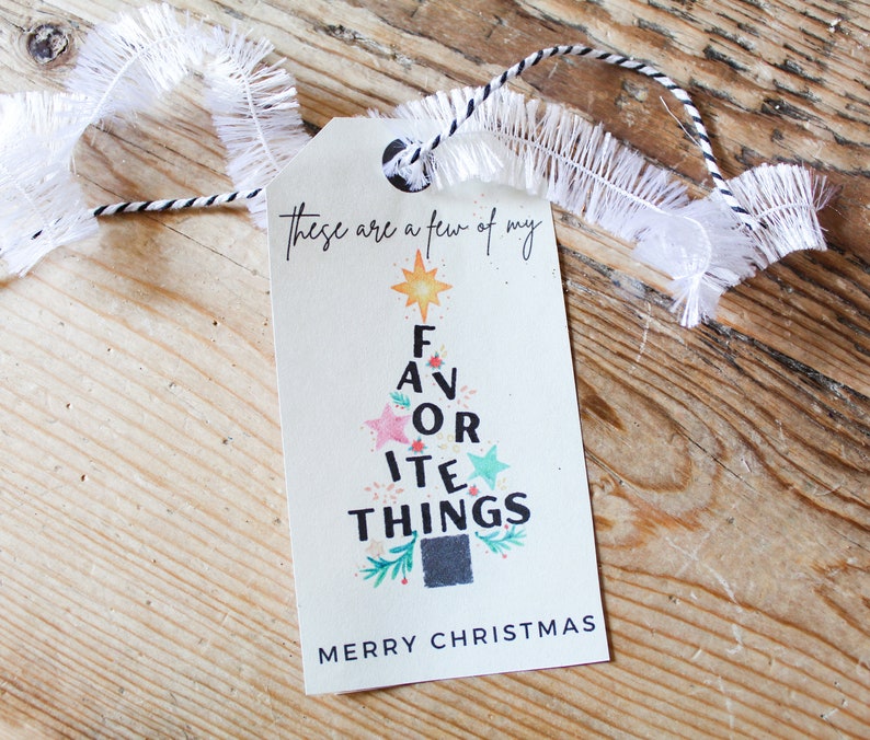 Op de afbeelding: Een wit cadeau-etiket met een zwart-wit koord. Het etiket heeft een kerstboomontwerp met de woorden "Dit zijn een paar van mijn favoriete dingen" en "Prettige Kerst".