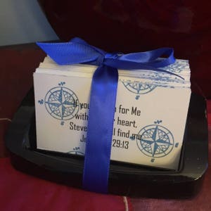 May include: A stack of white cards with blue compass designs and a blue ribbon tied around them. The cards have the text "If you search for Me with your heart, you will find Me" and "Jeremiah 29:13".