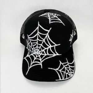 Puede incluir: Gorra de camionero negra con telarañas blancas y detalles de pedrería. La gorra tiene una parte trasera de malla negra y una visera curva. Un accesorio de moda para Halloween o uso diario.