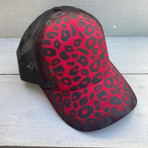 May include: A red and black trucker hat with a leopard print design. The hat has a mesh back and a black brim.