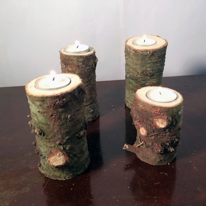 May include: Four rustic wooden candle holders with a natural bark finish. Each holder has a small white tea light candle inside.