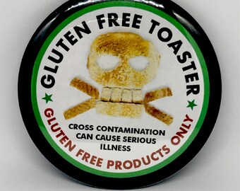 May include: A black and green round button with a white background. The button has a skull and crossbones made of bread with the text "Gluten Free Toaster Gluten Free Products Only" around the outside. The text "Cross Contamination Can Cause Serious Illness" is printed below the skull.