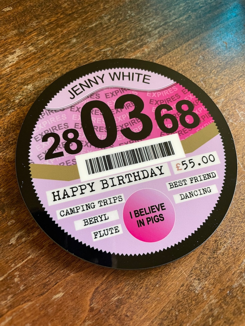 May include: A black and pink round sticker with the text "JENNY WHITE" and the date "28 03 68". The sticker also has the text "HAPPY BIRTHDAY" and "&pound;55.00". There are several other words on the sticker, including "CAMPING TRIPS", "BERYL", "FLUTE", "BEST FRIEND", "DANCING", and "I BELIEVE IN PIGS".