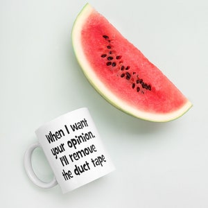 May include: White ceramic mug with black text that reads "When I want your opinion, I'll remove the duct tape". A slice of watermelon is in the background.