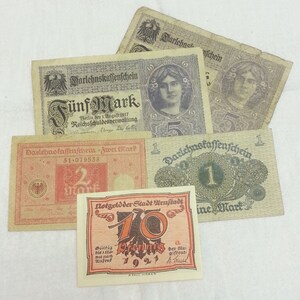 May include: A collection of vintage German banknotes, including a five-mark note, a two-mark note, and a one-mark note. There is also a small, red and orange note with the text "Notgeld der Stadt Urastadt 10 Pfennig 1921" printed on it.