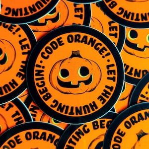 May include: A stack of round orange and black stickers with a pumpkin face and the text "Code Orange! Let the Hunting Begin!"