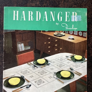 Könnte beinhalten: Ein Vintage-Stickbuch mit dem Titel "Hardanger by Penelope" mit einem Foto einer weißen Tischdecke mit geometrischem Muster, die auf einem Esstisch mit vier Stühlen und einer Holzkommode steht.