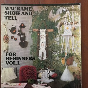 May include: A book titled "Macrame Show and Tell for Beginners Vol. 1" with a classic book logo. The cover features a variety of macrame projects, including wall hangings, plant hangers, and a pillow. The book includes 16 pages of Qwik Knots with over 200 illustrations of knots.