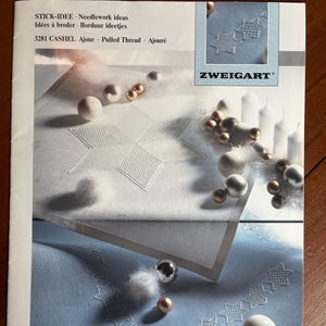 Puede incluir: Una revista que presenta ideas de bordado, con los logotipos "STICK-IDEE" y "ZWEIGART". La portada muestra ejemplos de patrones de estrellas bordadas sobre un fondo azul claro y blanco, junto con adornos decorativos.
