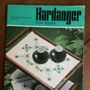 Peut inclure: Un livre vintage intitulé "Hardanger For Today" avec une couverture verte et une photo d'une nappe blanche avec des broderies vertes sur un chariot de service en bois. Le livre fait partie de la série Coats Sewing Group Book et est numéroté 1066.