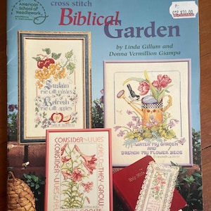 Può includere: Un libro di modelli a punto croce intitolato "Biblical Garden" di Linda Gillum e Donna Vermillion Giampa. La copertina presenta campioni a punto croce incorniciati di frutta, fiori e testo ispiratore. Sono visibili anche un libro rosso e un segnalibro decorativo.