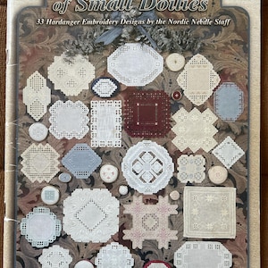 Peut inclure: La couverture du livre "The BIG Book of Small Doilies" présente 33 modèles de broderie Hardanger. La couverture montre divers motifs de napperons en blanc, crème et bleu clair, avec le titre et les informations sur l'auteur en haut et en bas.