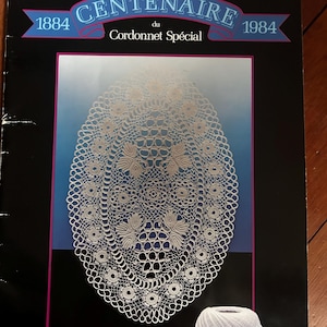 May include: A black booklet cover titled CENTENAIRE 1884 du Cordonnet Spécial 1984 featuring a white oval lace doily pattern with floral motifs against a blue gradient background and a ball of white thread at the bottom with the DMC logo.