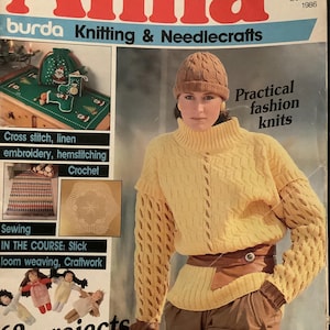 May include: Magazine cover featuring the title "Anna" in large red letters. The cover includes images of knitting and needlecraft projects, including cross-stitch, embroidery, and crochet. A woman is wearing a yellow knit sweater and a brown knit hat. The text "Practical fashion knits" is also visible.