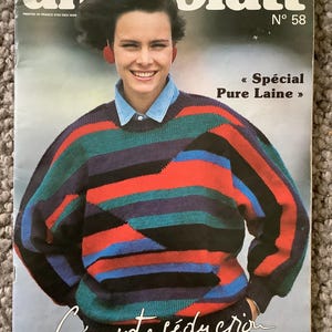 Può includere: Copertina della rivista Annablatt con una persona che indossa un maglione a righe rosse, verdi, blu e nere. Il titolo della rivista è in alto, con il testo « Spécial Pure Laine » e « Créez votre séduction ». La rivista è il n. 58.