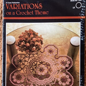 May include: A vintage book cover titled "VARIATIONS on a Crochet Theme" with a black background and orange accents. The image features a crocheted doily in shades of pink and burgundy, along with a bouquet of dried flowers and two cylindrical objects.