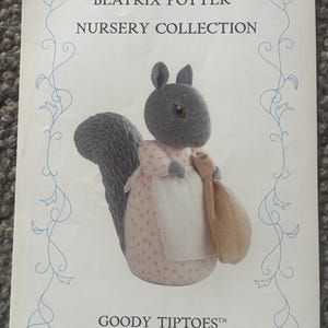 Puede incluir: Una página de la colección Beatrix Potter Nursery, con una ardilla tejida Goody Tiptoes. La ardilla es gris con un vestido rosa y blanco y una bolsa beige. La página tiene un borde floral azul.