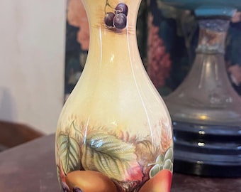 Peut inclure: Un petit vase en céramique de couleur crème avec un bord festonné. Le vase est décoré d'un motif peint de fruits, notamment des pêches, des raisins et des feuilles. Le fond est de couleur jaune clair.