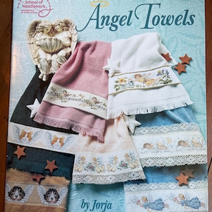 Può includere: Una collezione di asciugamani Angel Towels a punto croce, con vari colori e design. Gli asciugamani sono adornati con motivi di angeli ricamati, motivi floreali e il testo "SWEET DREAMS, ANGEL". La copertina mostra anche il testo "Angel Towels" e "by Jorja Hernandez".