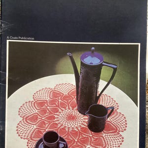 May include: A red crochet doily with a delicate pattern of hearts, displayed on a white table with a black teapot, creamer, and cup. The image is from a vintage crochet book titled "Crochet Collection: Ten Favourite Designs" with the book number "1342".